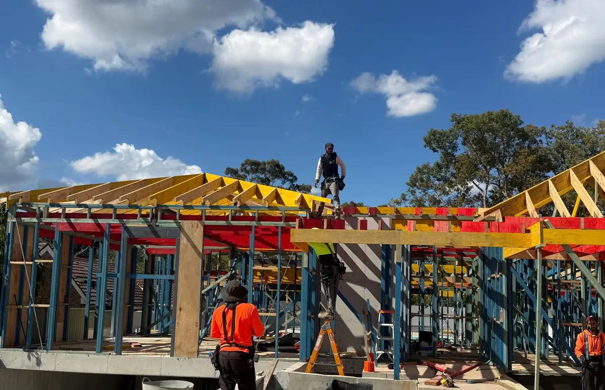Carpenters installing roof trusses on a timber frame over a concrete slab